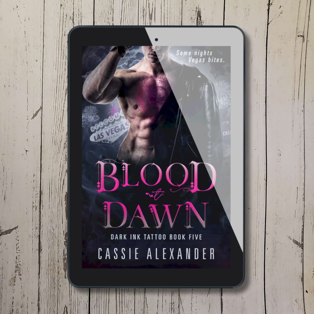 Tablet showing cover of "Blood at Dawn: Book 5" by Cassie Alexander with a shirtless man in a black leather jacket with a chest tattoo.
